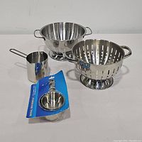 Overall view of 2 metal strainers and 2 sets of metal measuring cups included in the lot