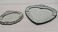 Two Venetian mirrors, one heart-shaped and one oval, showing front view on table.