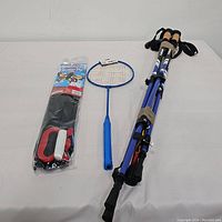 Photo showing the bundled items: butterfly kite kit still packaged, blue badminton racket, and three hiking poles folded together.