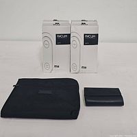 Four boxes of Pacum bags stacked, Waterfield black tote bag folded and flat, small black travel case folded.