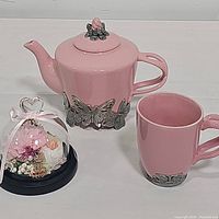 Full lot showing pink ceramic teapot, matching mug with metal butterflies, and preserved roses under glass dome