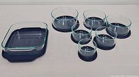 All seven Pyrex dishes with lids including 6 round bowls and one square baking dish.