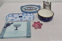 Blue and white religious-themed serving dishes including two trays with Menorah designs, bowl, pink star dish, and decorative plate with Hebrew lettering.