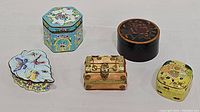 Four decorative trinket boxes grouped together on plain background: leaf-shaped butterfly design box, teal octagon box, treasure chest style box, and round lacquer box.