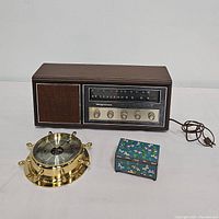 Three items on white background: vintage Magnavox radio, brass nautical barometer, and small blue jewelry box.