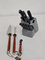Cuisinart knife block with ten knives and an included honing steel standing upright on white background, with vintage wood handled utensils beside it.