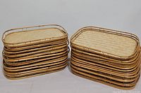 Stacked set of 20 rectangular woven bamboo and rattan framed serving lap trays, side view showing tray height and construction