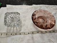 Two glass candle dishes on white fabric background, measuring tape shows size around 7 cm each