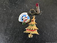 Photo of all three Christmas brooches: Christmas tree, Santa Claus 'Happy Holidays' pin, and candle with holly leaves.