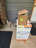 Photo showing original packaging boxes and hardware of the flush mount light fixtures outside a residential door.