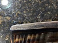 Close-up of the antique comb's silver casing showing engraved decoration and part of the comb's teeth.