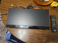 Top view of Sony Blu-ray DVD player alongside remote on wooden table with cables attached.