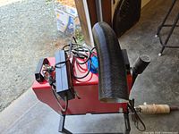 Front perspective view of red heater unit with black flexible exhaust hose and power cables on top.