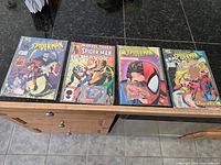 Four vintage Spider-Man comic books laid out on a dark surface, each inside clear protective sleeves, showing colorful covers with Spider-Man and other characters.