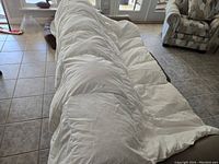 Full view of the white quilt duvet draped over a couch in a living room with tiled floor and furniture.