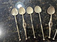 Five vintage/antique handmade spoons laid out on dark granite countertop showing general condition and style