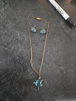 Overall view of the necklace and earrings on a dark textured surface, includes a marker for scale