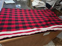 Full view of the knitted red and black checkered throw blanket laid out covering a brown surface, showing size and pattern.