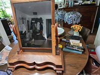 Large wooden framed rectangular mirror on table showing overall shape, stand and base with carved feet detail.