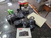 Lot overview showing cameras, film rolls, carrying case, and book on table