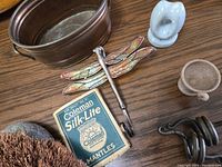 Photo showing brass planter, metal dragonfly, ceramic ring holder, pottery cup, cast iron hook, Coleman Silk-Lite mantles box
