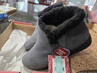 Grey Mukluks boots with black faux fur lining inside the original box with tags attached showing memory foam and water repellent features.
