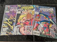 Three vintage Spiderman comics, each in protective sleeves showing front covers and collectible cards inside.