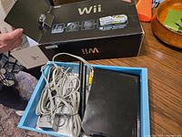 Photo showing original Nintendo Wii box with partial view of contents inside including wires and console.