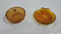 Photo showing top-down side view of the vintage amber glass lidded dish and the shell-shaped candy dish on quilted white surface.