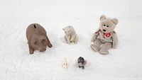 Lot grouping showing the brown piggy bank, beige dog figurine, beige stuffed teddy bear, and two small animal figurines (beige and black).