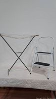 Folding clothes dryer rack and two-step stool side by side against white backdrop.