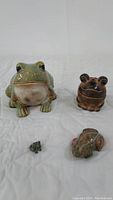 Front view of four frog figurines on a white background, showing different sizes and colors.