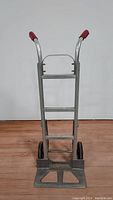 Front view of used aluminum hand truck with red handle grips and foldable toe plate.