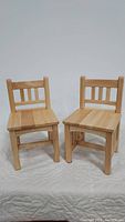 Front angle of two small wooden kids chairs showing slatted backrest and seats
