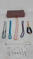 Top view of assorted beaded necklaces and the decorative jewelry box on a white surface.