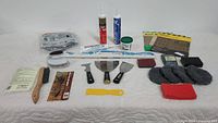Array of assorted sanding and cleaning tools including sanding discs, sanding sheets, scrapers, brushes, sealant tubes, sponge, and a small container.