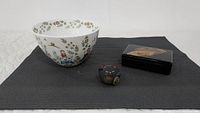 Top-down and angled photo of all three items on a black textured mat: the Scandinavian-style bowl, Japanese lacquer box, and Lucky Cat figurine