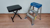 Small step ladder and cushioned keyboard bench side by side on floor