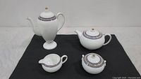 Full view of four-piece set laid on black mat: coffee pot, tea pot, sugar bowl, and creamer showing overall design and condition.