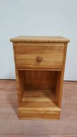 Front view of the wood nightstand showing one drawer with a round wooden knob and an open shelf below.