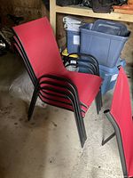 Four stacking red patio chairs with black metal frames shown stacked and one chair separate, taken in a dark indoor space.