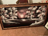 Velvet painting artwork showing riverside landscape with trees in dark colors with pink highlights