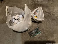 Multiple used golf balls, golf tees, and pencils inside plastic bags on concrete floor.