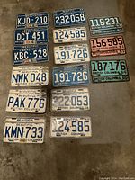 Photo showing 16 British Columbia license plates laid out on concrete surface in traffic worn condition.