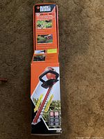 Photo showing boxed hedge trimmer with product info on box in orange and black colors.