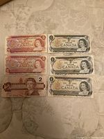 Top view of three $1 Canadian bills laid out showing front side with Queen Elizabeth II portrait and serial numbers.