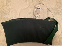 Green massage cushion with attached strap and electric cord for power supply, laid flat on a surface.