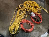 Photo showing the three extension cords: two orange and one yellow, coiled on a concrete floor.