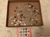 Top-down photo of many assorted foreign coins in a cardboard tray including a coin display card with multiple organized coins.