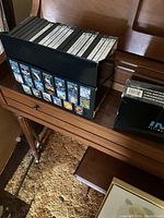 Black cardboard holder on a wooden surface containing approximately 19 DVDs with visible titles and cover images related to IMAX documentaries.